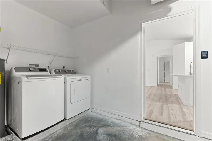 Washroom featuring washing machine and clothes dryer, unfinished concrete floors, and water heater