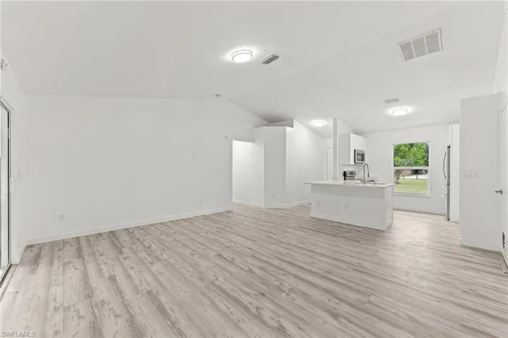 Unfurnished living room with lofted ceiling and light wood-type flooring