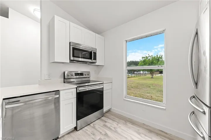 Kitchen with appliances with stainless steel finishes, white cabinetry, lofted ceiling, light wood-style floors, and light stone counters