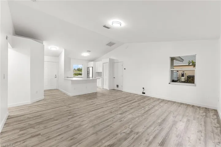 Unfurnished living room with light wood finished floors and vaulted ceiling