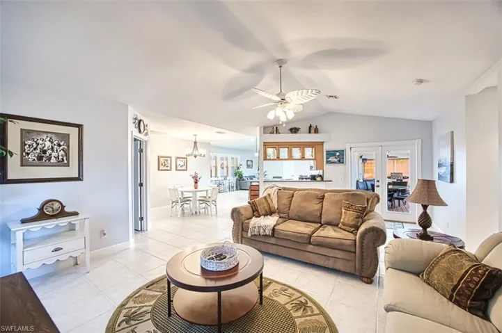 Living room with vaulted ceiling, a ceiling fan, light tile patterned floors, a chandelier, and baseboards