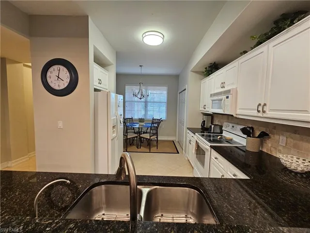 Kitchen with white appliances, decorative backsplash, white cabinetry, a chandelier, and dark stone counters