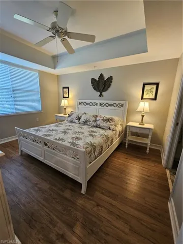 Bedroom with a raised ceiling, dark wood-style floors, and ceiling fan