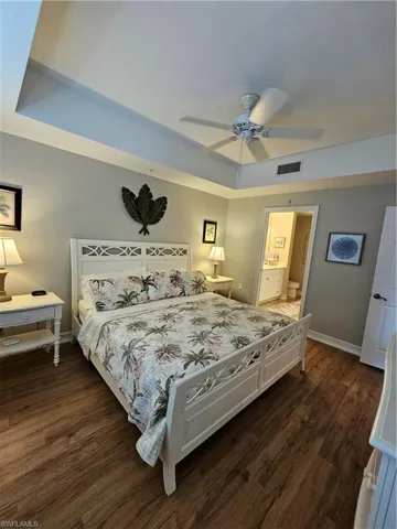 Bedroom featuring dark wood finished floors, a raised ceiling, a ceiling fan, and ensuite bath