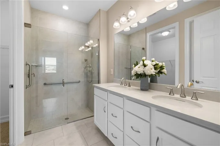 Primary Bathroom with walk in shower with grab bar and floating shelf, double sinks, walk-in closet