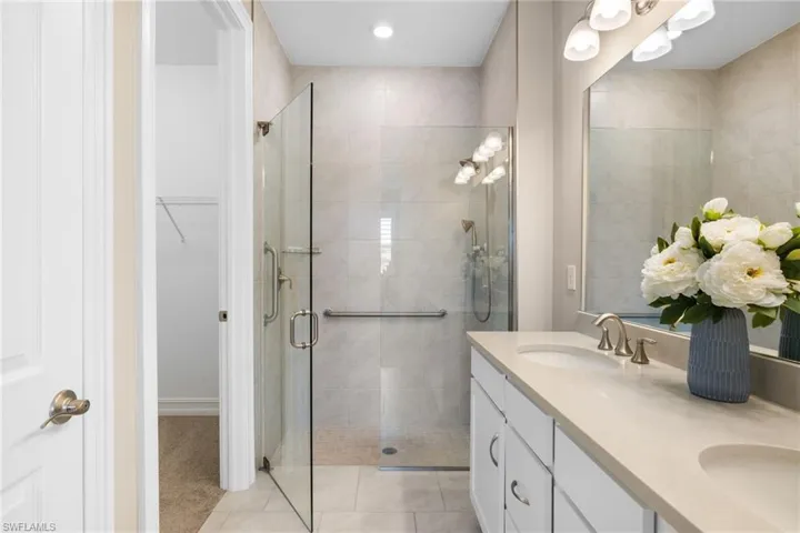 Primary Bathroom with walk in shower with grab bar and floating shelf, double sinks, walk-in closet