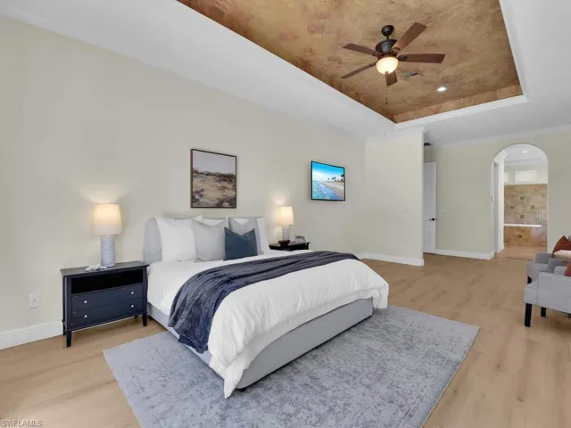 Bedroom featuring a tray ceiling, light wood-type flooring, baseboards, and arched walkways