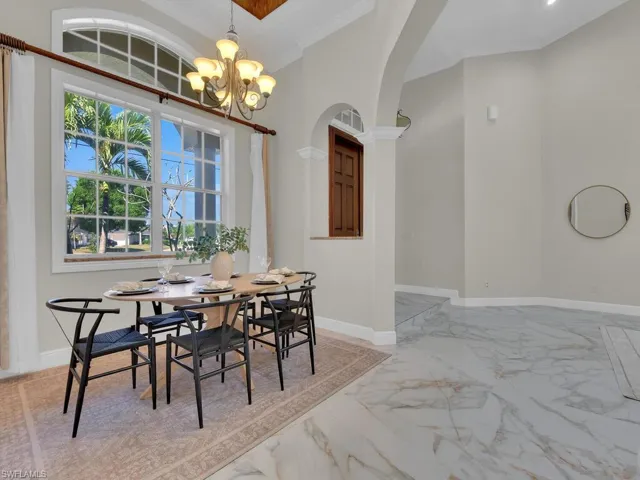 Dining area featuring light marble finish flooring, arched walkways, crown molding, a chandelier, and baseboards