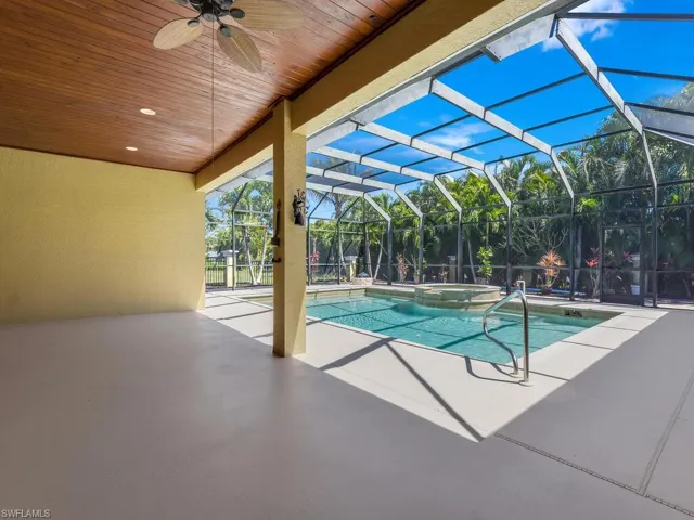 View of pool featuring a ceiling fan, a patio, a pool with connected hot tub, and glass enclosure