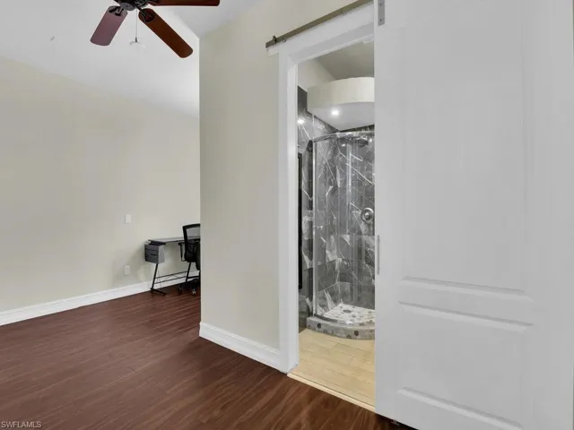 Empty room with a barn door, wood finished floors, a ceiling fan, and baseboards