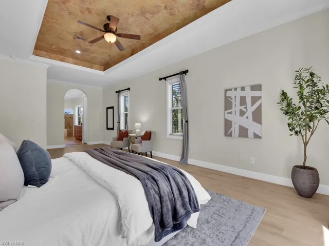 Bedroom featuring a raised ceiling, arched walkways, wood finished floors, and baseboards