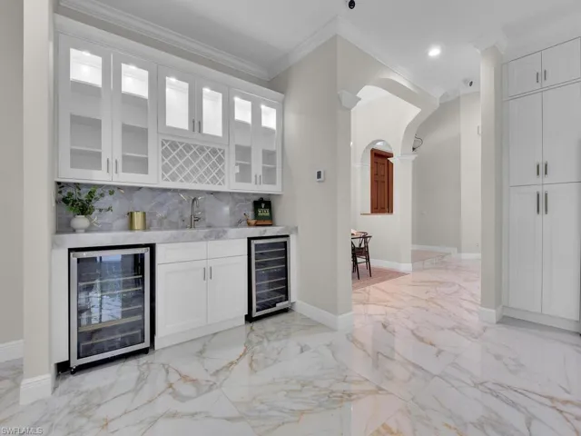 Indoor wet bar with wine cooler, light marble finish flooring, crown molding, backsplash, and arched walkways