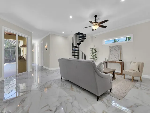 Living room featuring healthy amount of natural light, light marble finish flooring, stairs, crown molding, and a ceiling fan