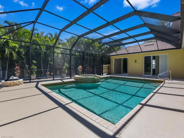 View of swimming pool featuring a patio, a pool with connected hot tub, glass enclosure, and a fire pit