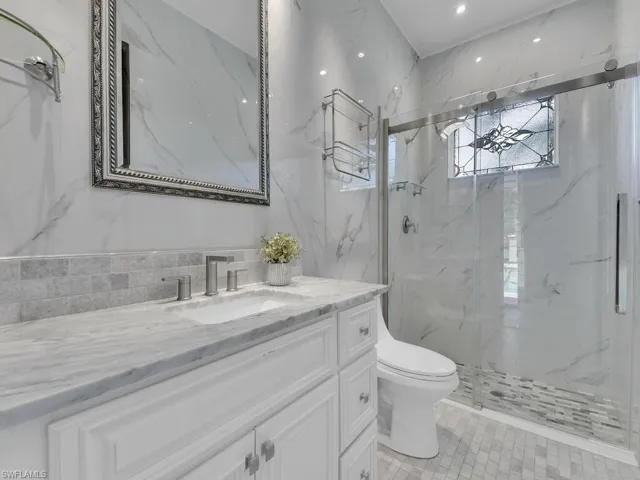 Bathroom featuring a marble finish shower, toilet, vanity, recessed lighting, and tile walls