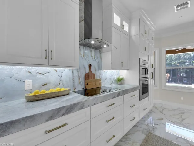 Kitchen with wall chimney range hood, black electric cooktop, backsplash, white cabinets, and double oven