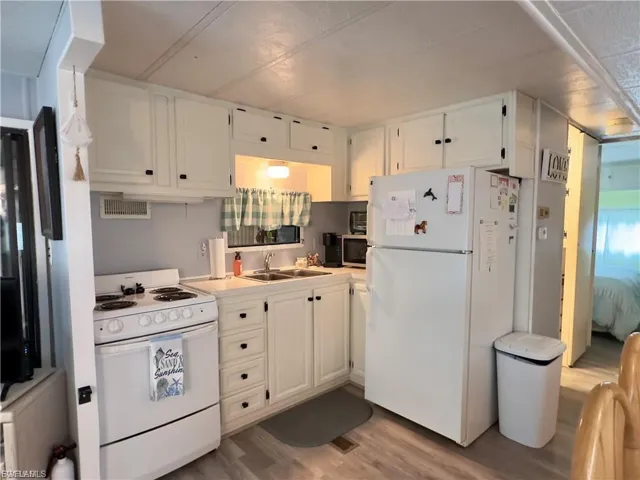 Kitchen with white appliances, white cabinets, light wood finished floors, and light countertops