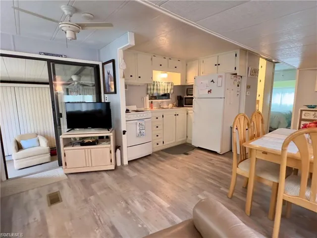 Kitchen featuring white appliances, light countertops, light wood-style floors, a ceiling fan, and white cabinets