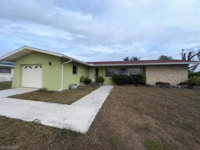 Ranch-style home with a front lawn, stucco siding, an attached garage, and driveway