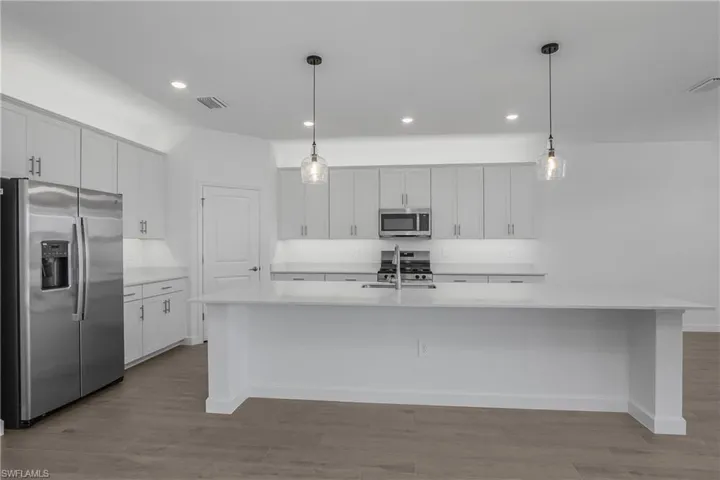 Kitchen with custom backsplash, over and under cabinet lighting, white cabinets, a center island with sink, and decorative light fixtures.