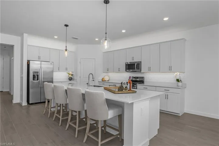 Kitchen with stainless steel appliances, a breakfast bar, wood finish floors, a center island with sink, and white cabinets. (photo is from staged home in community)