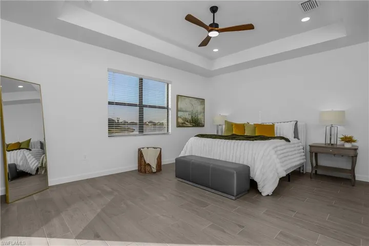 Bedroom with a raised ceiling, recessed lighting, ceiling fan, and wood finish floors. (photo is from staged home in community)