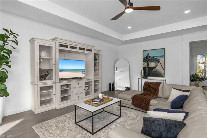 Living room with a ceiling fan, wood finished floors, recessed lighting, and a tray ceiling. (photo is from staged home in community)