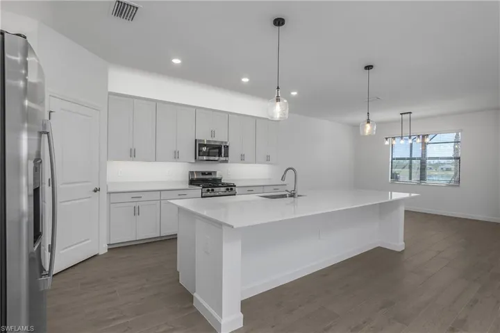 Kitchen featuring a kitchen bar, decorative light fixtures, stainless steel appliances, a center island with sink, and light wood-look tile flooring.