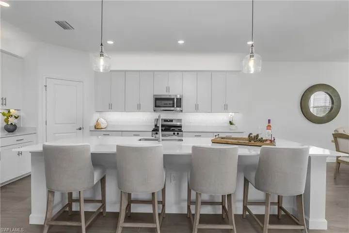 Kitchen with custom backsplash, over and under cabinet lighting, white cabinets, a center island with sink, and decorative light fixtures. (photo from virtually staged home in the community)