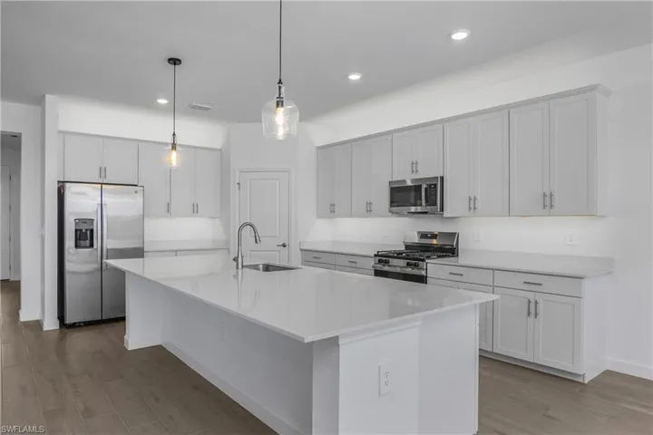 Kitchen with stainless steel appliances, a breakfast bar, wood finish floors, a center island with sink, and white cabinets.