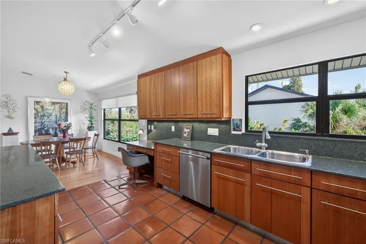 Kitchen featuring dark stone countertops, wood finish cabinetry, dishwasher, tasteful backsplash, and rail lighting