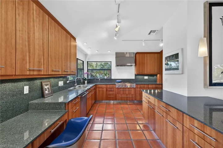 Kitchen featuring dark stone countertops, wood finish cabinets, track lighting, modern cabinets, and backsplash