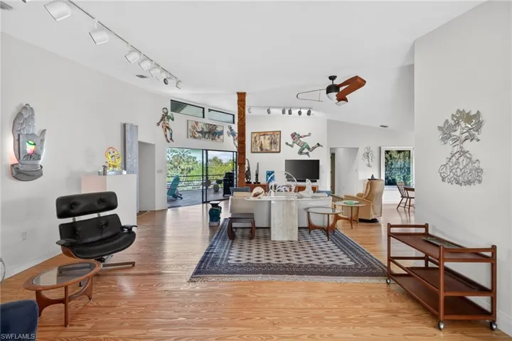 Living room with rail lighting, a ceiling fan, light wood finished floors, lofted ceiling, and healthy amount of natural light
