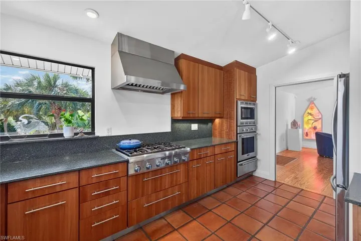 Kitchen with dark stone counters, wood finish cabinets, modern cabinets, rail lighting, and stainless steel appliances