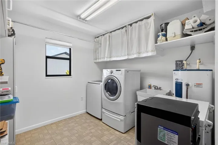 Laundry room with electric water heater, washer and clothes dryer, and brick patterned floors