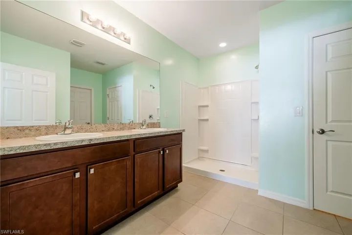 Bathroom featuring two sinks, tiled shower, tile patterned flooring, and double vanity