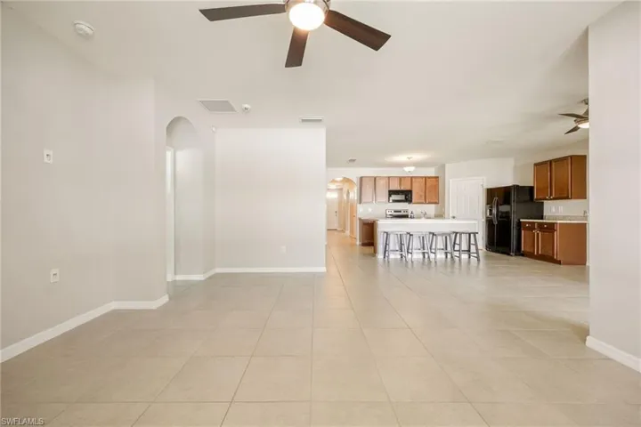 Unfurnished living room featuring arched walkways, visible vents, baseboards, and ceiling fan