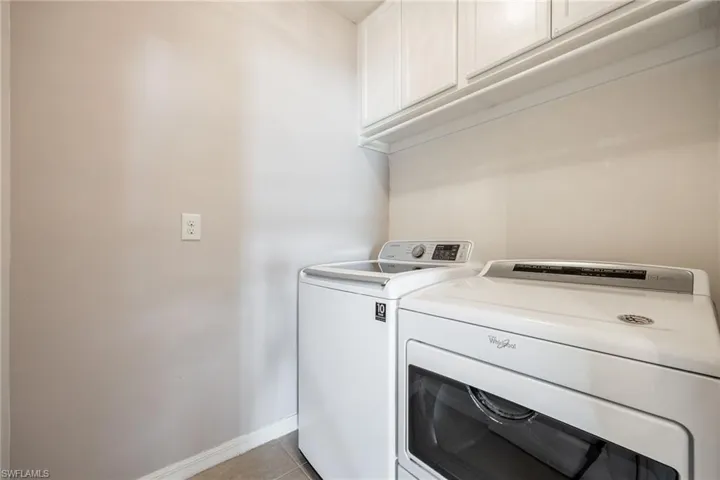 Laundry area featuring cabinet space, independent washer and dryer, light tile patterned flooring, and baseboards