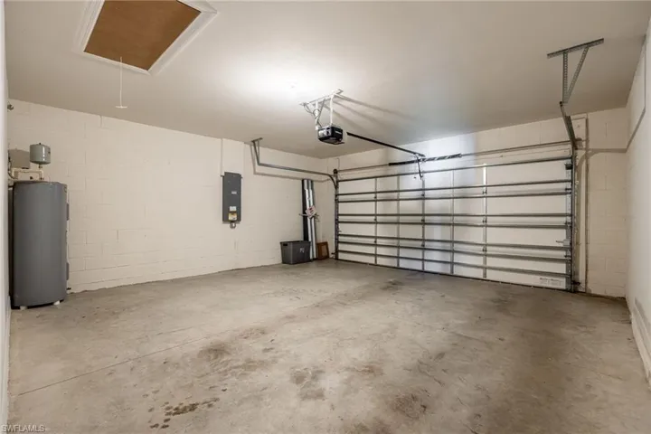Garage with electric water heater, electric panel, a garage door opener, and concrete block wall