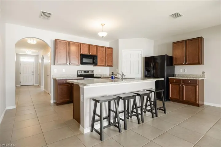 Kitchen featuring arched walkways, visible vents, black appliances, and a kitchen breakfast bar