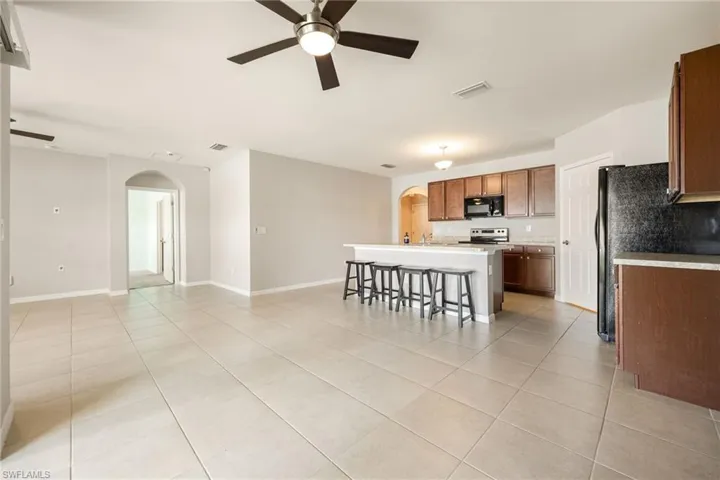 Kitchen featuring stainless steel electric range oven, light tile patterned floors, arched walkways, a ceiling fan, and black microwave