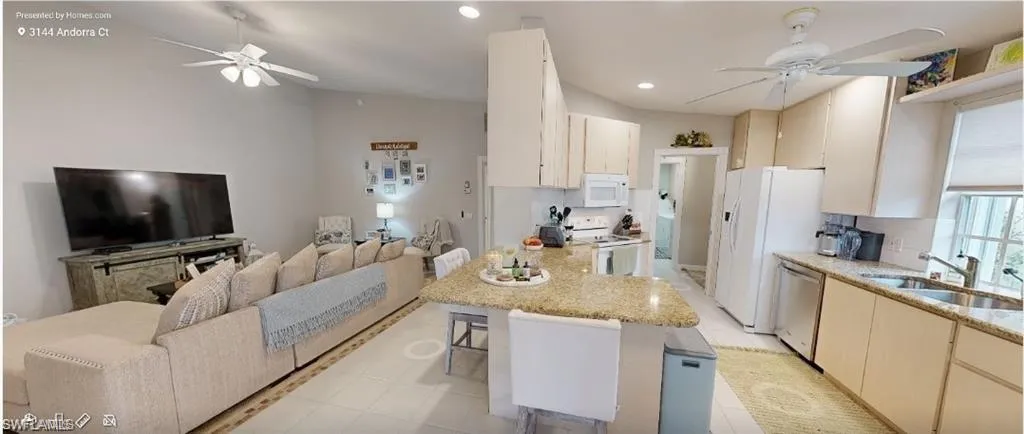 Kitchen with a ceiling fan, open floor plan, a peninsula, a breakfast bar, and white appliances