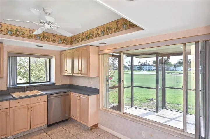 Kitchen featuring stainless steel dishwasher, light brown cabinetry, and dark countertops