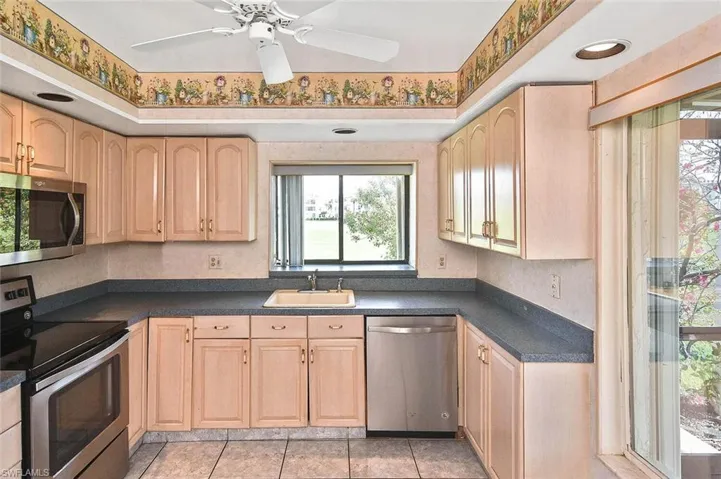 Kitchen with stainless steel appliances, light brown cabinets, dark countertops, and a ceiling fan