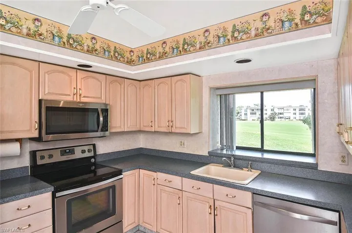 Kitchen with stainless steel appliances, light brown cabinetry, dark countertops, and a ceiling fan