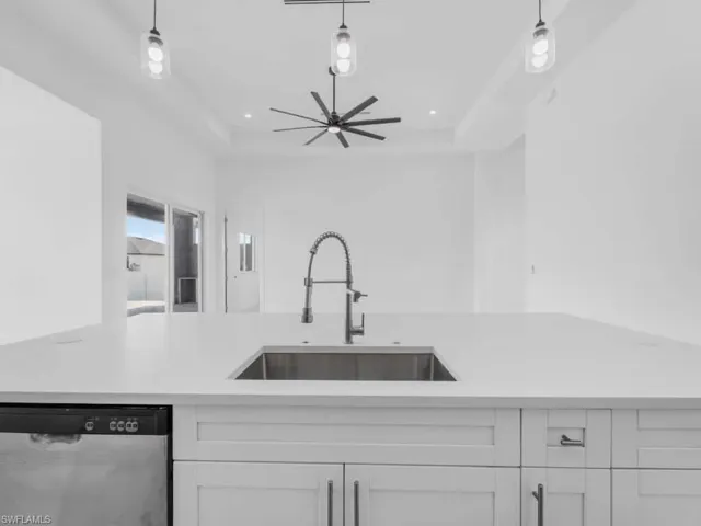 Kitchen featuring stainless steel dishwasher, light countertops, a tray ceiling, a ceiling fan, and white cabinets