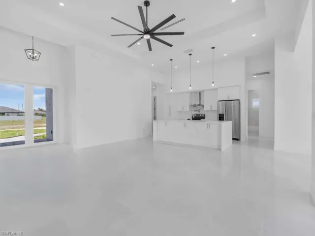Unfurnished living room featuring a raised ceiling, a ceiling fan, a chandelier, and recessed lighting