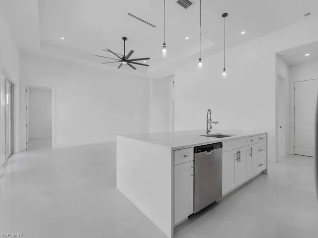 Kitchen with white cabinets, stainless steel dishwasher, hanging light fixtures, light countertops, and a center island with sink