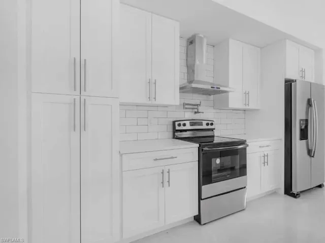 Kitchen with appliances with stainless steel finishes, wall chimney exhaust hood, light countertops, white cabinetry, and decorative backsplash