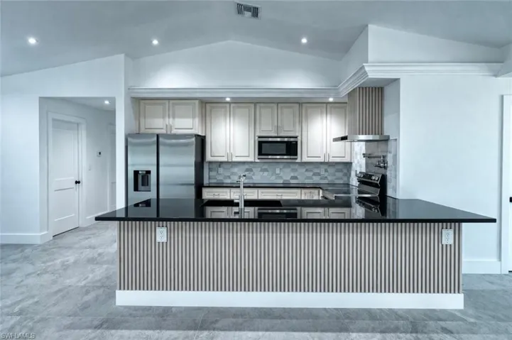 Kitchen with stainless steel appliances, dark stone countertops, vaulted ceiling, a peninsula, and decorative backsplash